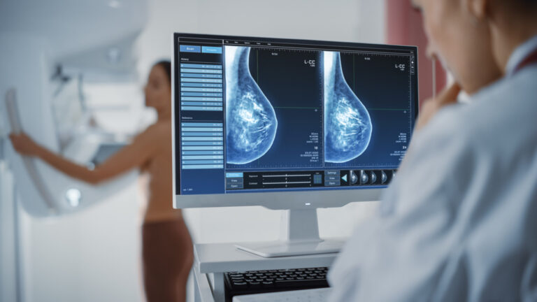 Technician looking at a computer screen while patient us undergoing a mammography screening