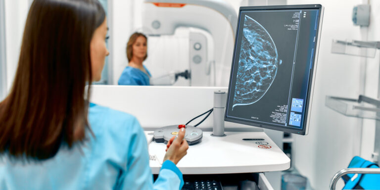 Patient undergoes a screening procedure for a mammogram, while the technician looks at the scan
