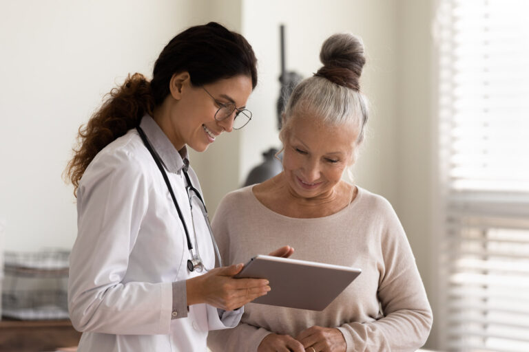 Happy female doctor and senior patient look at tablet screen discuss treatment or therapy on tablet.