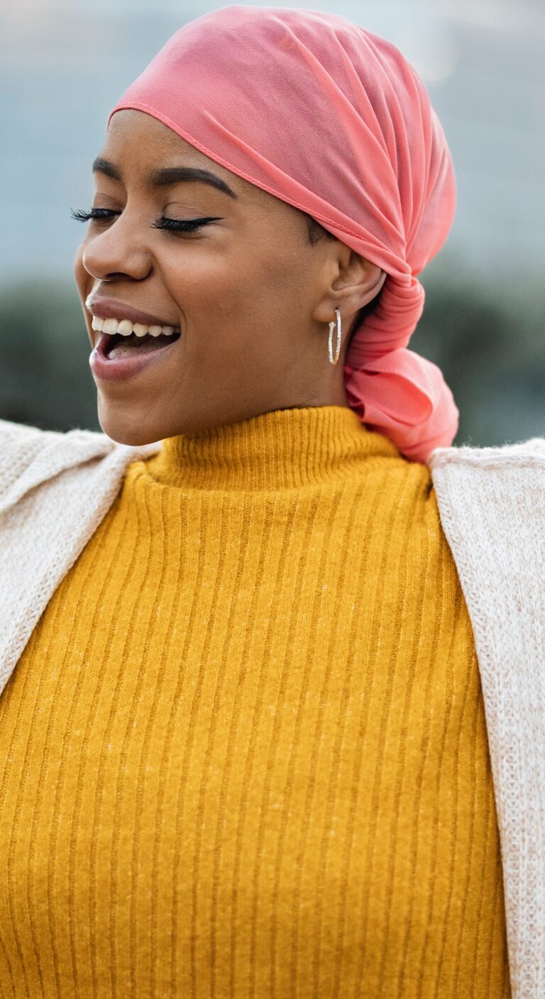 Latina woman, fighting breast cancer, wears a pink scarf, and clenches her arms as a survivor fighter