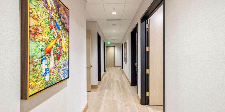 Bright, modern hallway with light wood flooring, cream-colored walls, several open doorways, and a colorful painting of koi fish on the left wall.