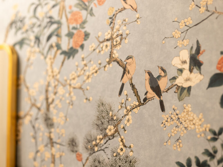Detail of decorative wallpaper featuring illustrated birds perched on flowering branches, with blossoms and foliage in muted tones.
