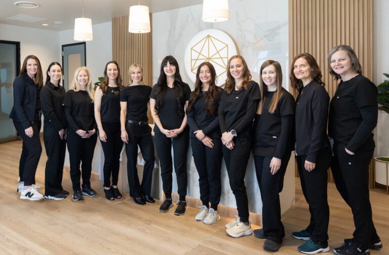 Lyra team dressed in black uniforms or outfits stand side by side, smiling, in a modern office with wood flooring, pendant lights, and a geometric logo on the wall behind them.