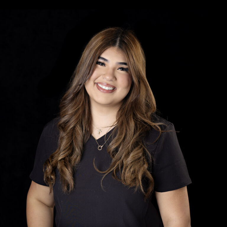 Smiling woman with long, wavy brown hair wearing a black shirt, photographed against a plain black background.